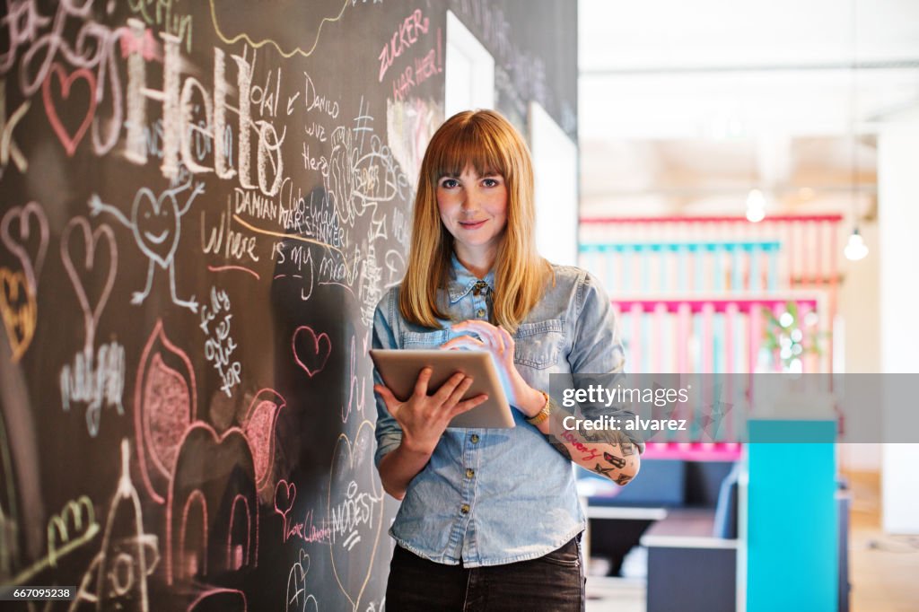 Businesswoman using digital tablet by blackboard