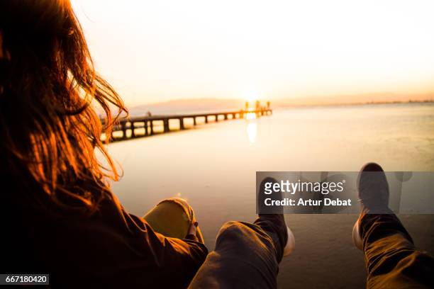 beautiful couple in love sitting and contemplating the sunset over the ebro delta in the mediterranean sea from wood pier and stunning sunlight during a weekend travel in the region. - ebro delta stock pictures, royalty-free photos & images