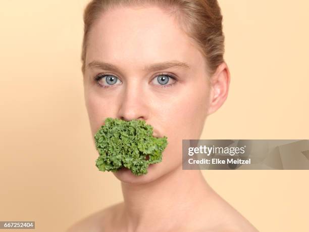 woman with kale in her mouth - restraining device stockfoto's en -beelden