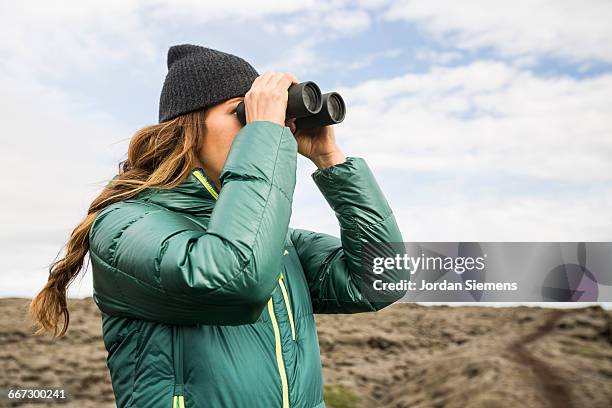 a woman peering through pair of binoculars. - looking through binoculars stock pictures, royalty-free photos & images