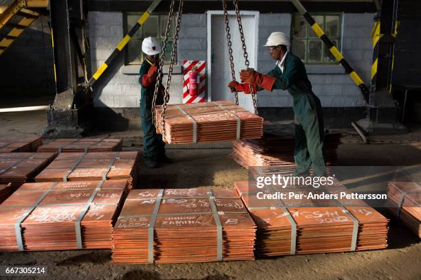 Workers move batches of copper sheets, which are stored in a warehouse and wait to be loaded on trucks on July 6, 2016 in Mufulira, Zambia. The...