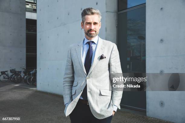 nachdenklicher geschäftsmann steht mit hand in der tasche gegen moderne architektur - grauer-anzug stock-fotos und bilder