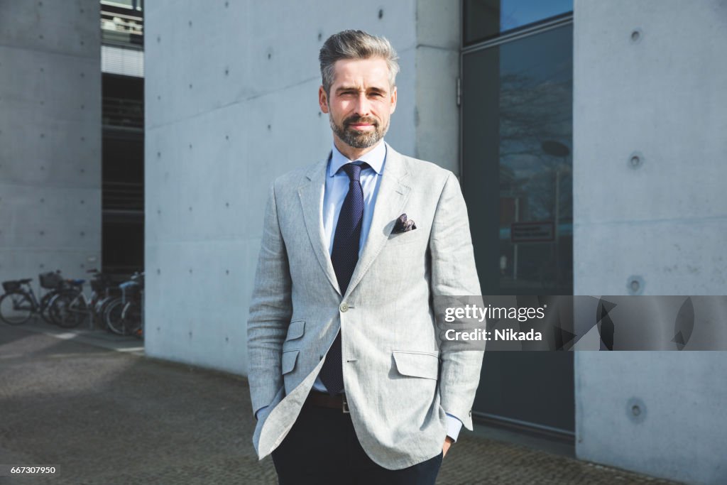 Thoughtful businessman standing with hand in pocket against modern architecture