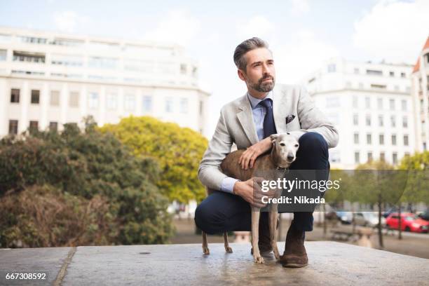 side view of businessman crouching by dog at doorway - well dressed dog stock pictures, royalty-free photos & images