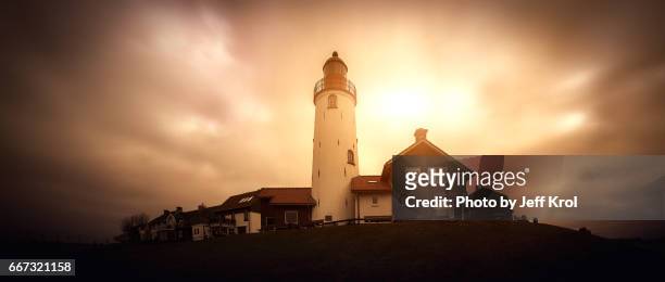panoramic view of a lighthouse on a hill with houses, windy sky with sun coming through the clouds. - zonsondergang 個照片及圖片檔