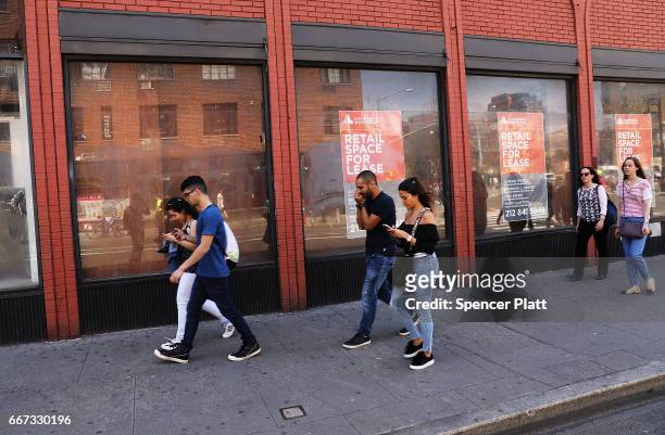People walk by a long empty store front in a trendy West Village neighborhood on April 11, 2017 in New York City. Many residents and tourists alike...