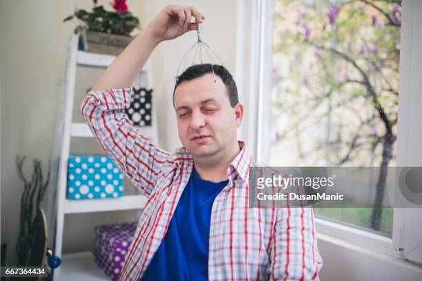 young attractive man at modern office desk, massaging temples to forget about constant headaches - massager stock pictures, royalty-free photos & images