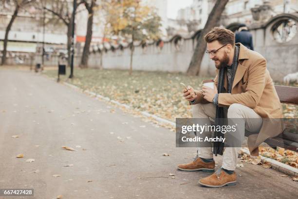 man texting message in the public park - smirking stock pictures, royalty-free photos & images