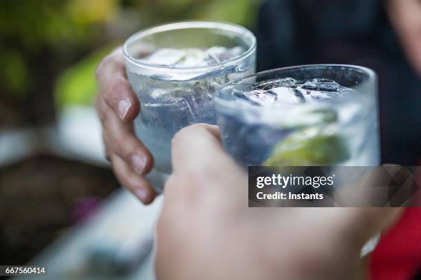 feier-konzept mit hand nahaufnahme von ein paar feiert den beginn ihrer ferien mit jedem ein gin & tonikum. - eiswürfel glas stock-fotos und bilder