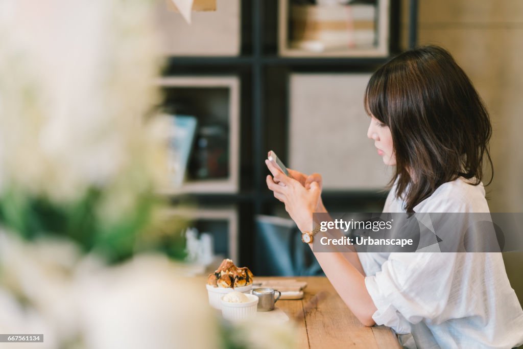 Beautiful Asian girl using smartphone at cafe with chocolate toast, ice cream, and milk syrup. Coffee shop dessert and modern casual lifestyle or mobile phone technology concept. With copy space