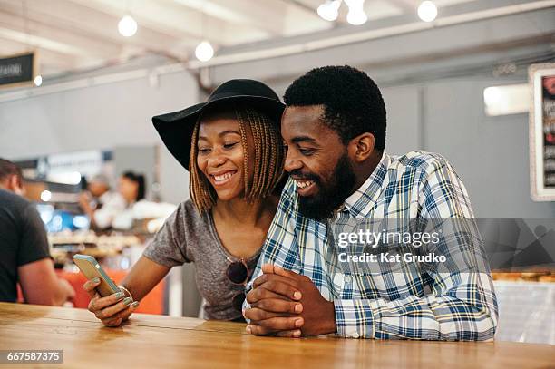 young ethnic african couple looking at mobile device in trendy market in braamfontein johannesburg south africa - johannesburg south africa stock pictures, royalty-free photos & images