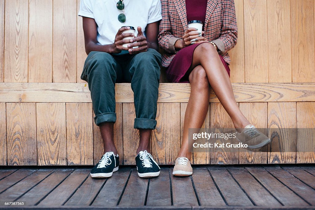 Young trendy ethnic African couple sitting on bench outside coffee shop in trendy street in Braamfontein Johannesburg South Africa