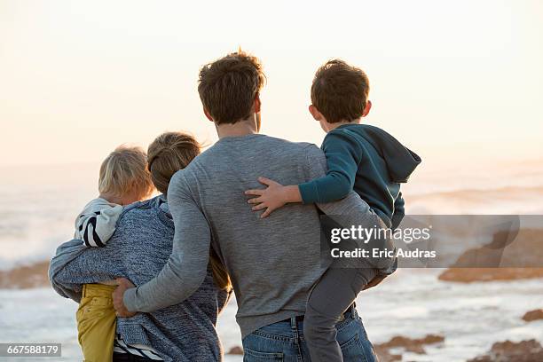 happy young family looking at sea on the beach at sunset - four people foto e immagini stock