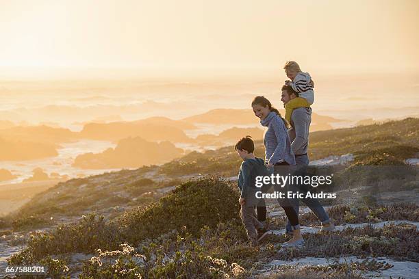 happy young family walking on the beach at sunset - young family foto e immagini stock