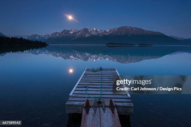 boat dock with a full moon rising over the chigmit mountains at lake clark in lake clark national park and preserve, alaska. - chigmit mountains stock pictures, royalty-free photos & images