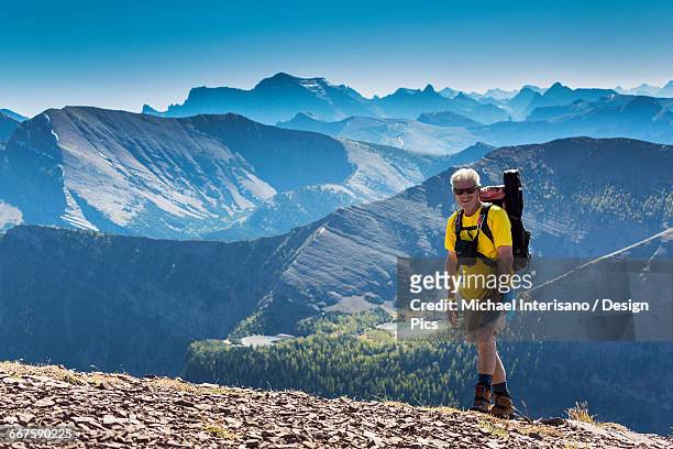 male hiker ascending a rocky peak with mountain ranges and lakes in the background - waterton lakes national park stockfoto's en -beelden