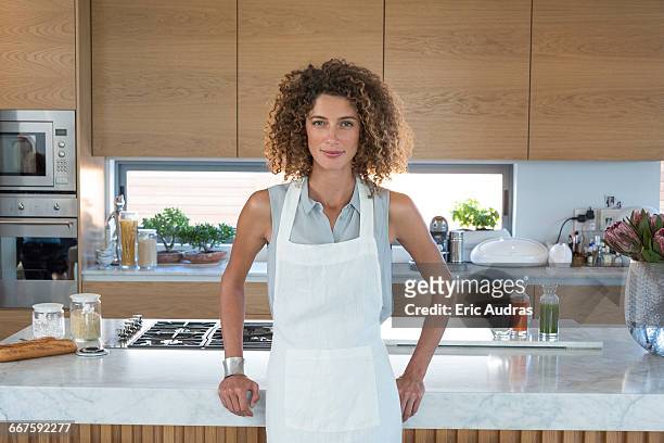 portrait of a young woman leaning against kitchen counter - apron stock pictures, royalty-free photos & images