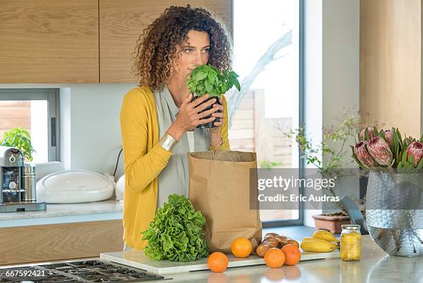 beautiful woman smelling houseplant in the kitchen - brot einkaufen stock-fotos und bilder