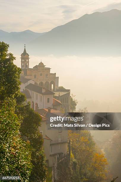 fog sets in over a church and alpine lake - locarno stock pictures, royalty-free photos & images