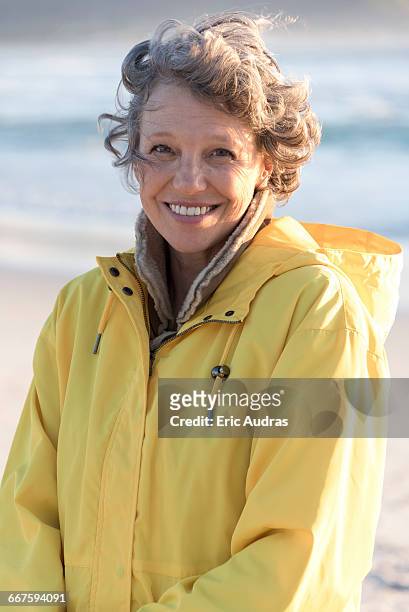 portrait of happy mature woman smiling on the beach - raincoat stockfoto's en -beelden