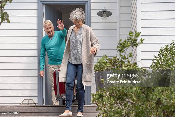 happy senior man waving to his wife with suitcase on staircase - waving goodbye stock pictures, royalty-free photos & images
