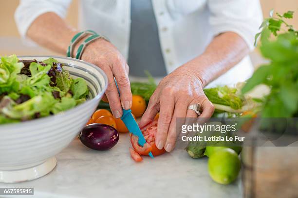 senior woman cutting vegetables in kitchen - senior cooking stock pictures, royalty-free photos & images