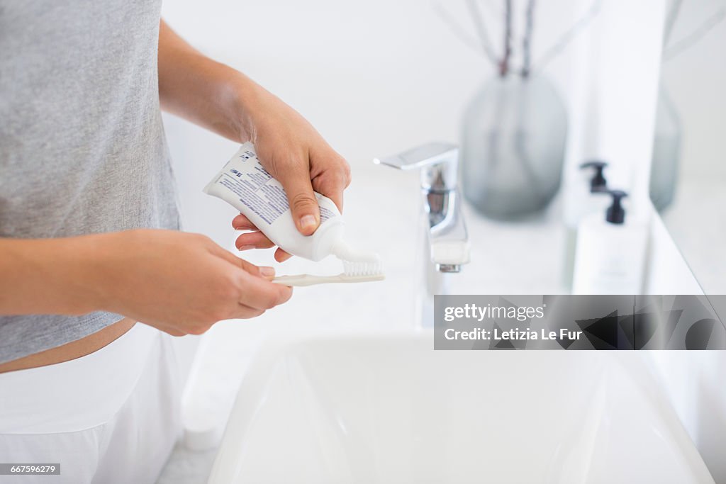 Woman squeezes the toothpaste from a tube on toothbrush