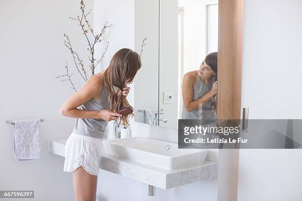 woman combing hair in a bathroom - bathroom sink stock-fotos und bilder