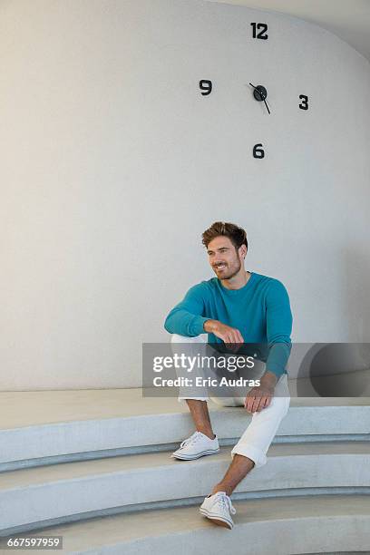 happy young man sitting on steps at home - man stairs sitting stock-fotos und bilder