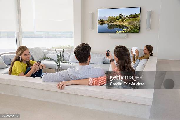 rear view of couple watching television with their daughters busy in different activities - familia viendo television fotografías e imágenes de stock