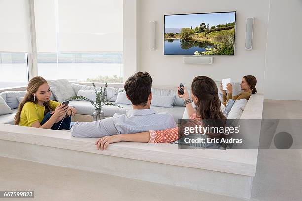 rear view of couple watching television with their daughters busy in different activities - back cushion stock pictures, royalty-free photos & images