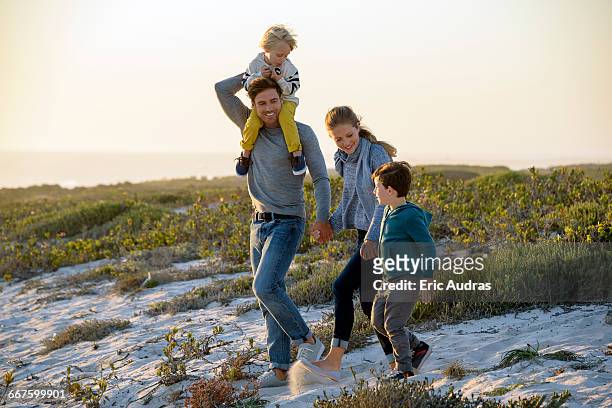 happy young family walking on the beach at sunset - young family stock pictures, royalty-free photos & images