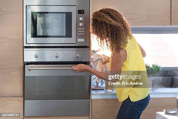 young woman opening door of an oven - microwave photos et images de collection