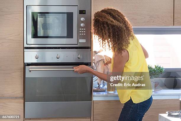 young woman opening door of an oven - microwave oven stockfoto's en -beelden