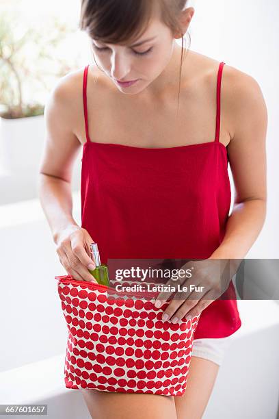 beautiful woman taking moisturizer bottle from make-up bag - beauty case stockfoto's en -beelden