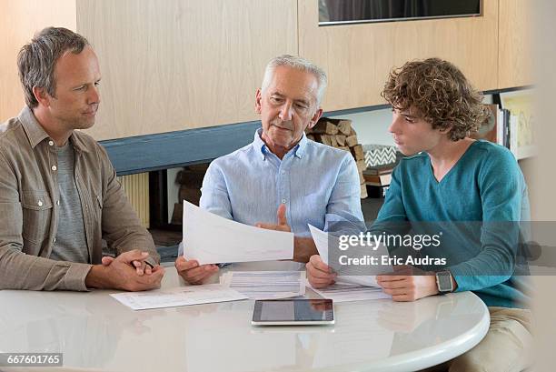 senior man doing paperwork with son and grandson in a living room - großvater vater sohn business stock-fotos und bilder