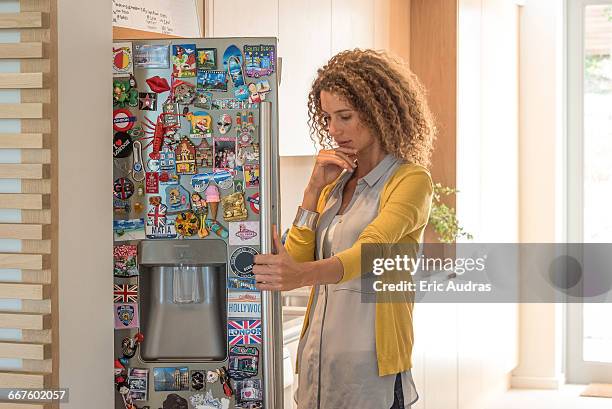 young woman looking into refrigerator - magnet stock-fotos und bilder