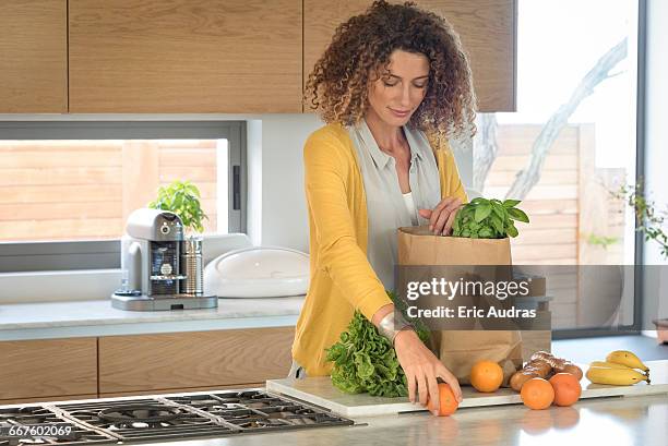 woman taking out food from a paper bag in the kitchen - frau tüte einkaufen stock-fotos und bilder