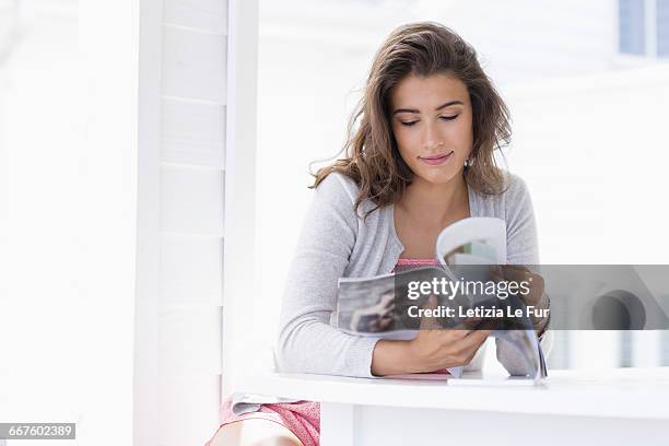 young woman reading magazine at home - holding magazine stock-fotos und bilder