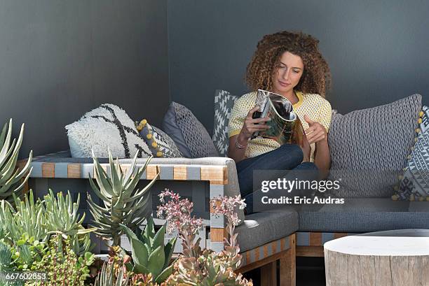 woman sitting on a couch and reading a magazine - magazine foto e immagini stock