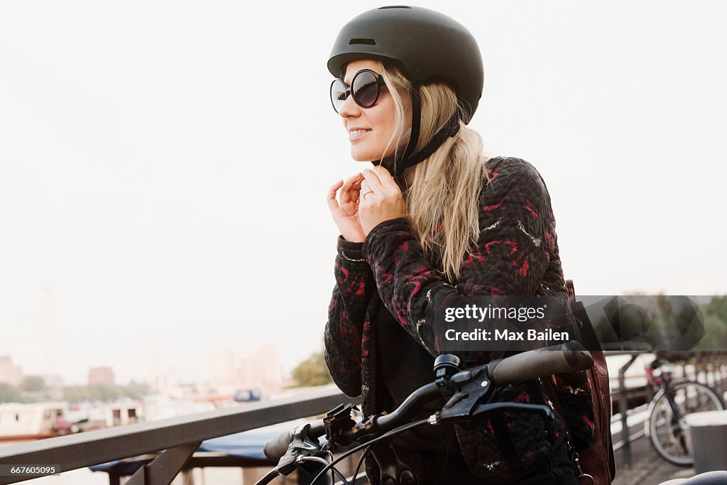 Young woman outdoors, putting on helmet, ready to ride bicycle