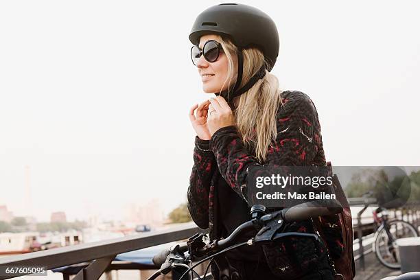 young woman outdoors, putting on helmet, ready to ride bicycle - cycling helmet stock pictures, royalty-free photos & images