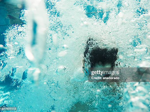 underwater view of boy jumping into a swimming pool - adem inhouden stockfoto's en -beelden