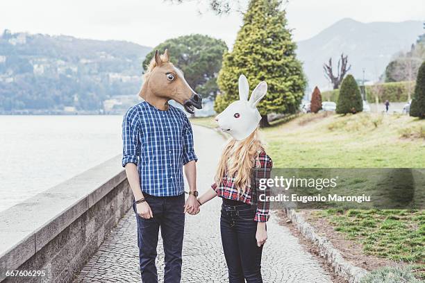 couple wearing horse and rabbit masks holding hands, lake como, italy - funny mask stockfoto's en -beelden