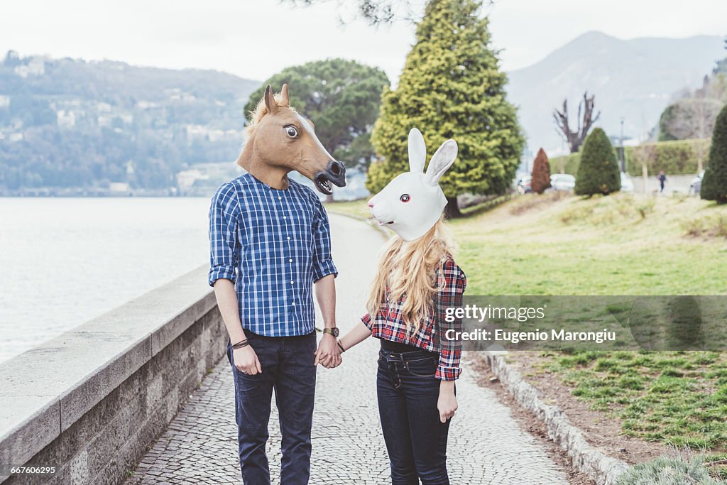 Couple wearing horse and rabbit masks holding hands, Lake Como, Italy