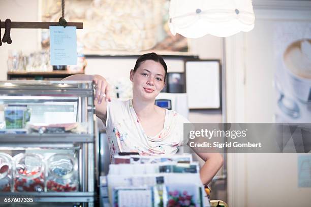 portrait of young female shop assistant leaning on corner shop counter - convenience store counter stockfoto's en -beelden