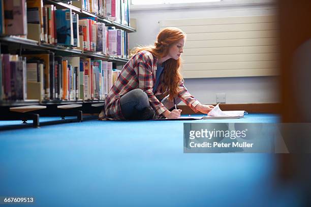 young female college student writing notes on library floor - surrey england stock-fotos und bilder