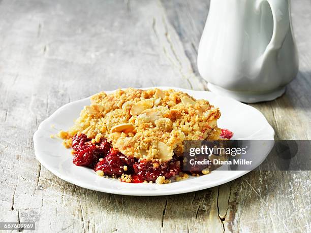 sour cherry and almond crumble pudding on white plate, white washed rustic wooden table - degeneration stock pictures, royalty-free photos & images