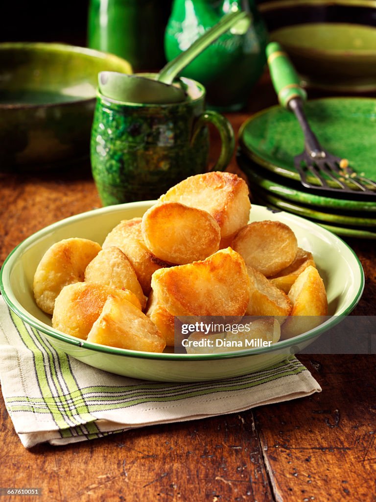 Roast potatoes in vintage green bowl, plates and fork, rustic wooden table