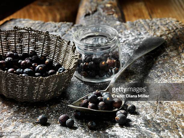 juniper berries in small glass jar, metal vintage spoon and woven basket, rustic wooden chopping board - wacholderbeeren stock-fotos und bilder